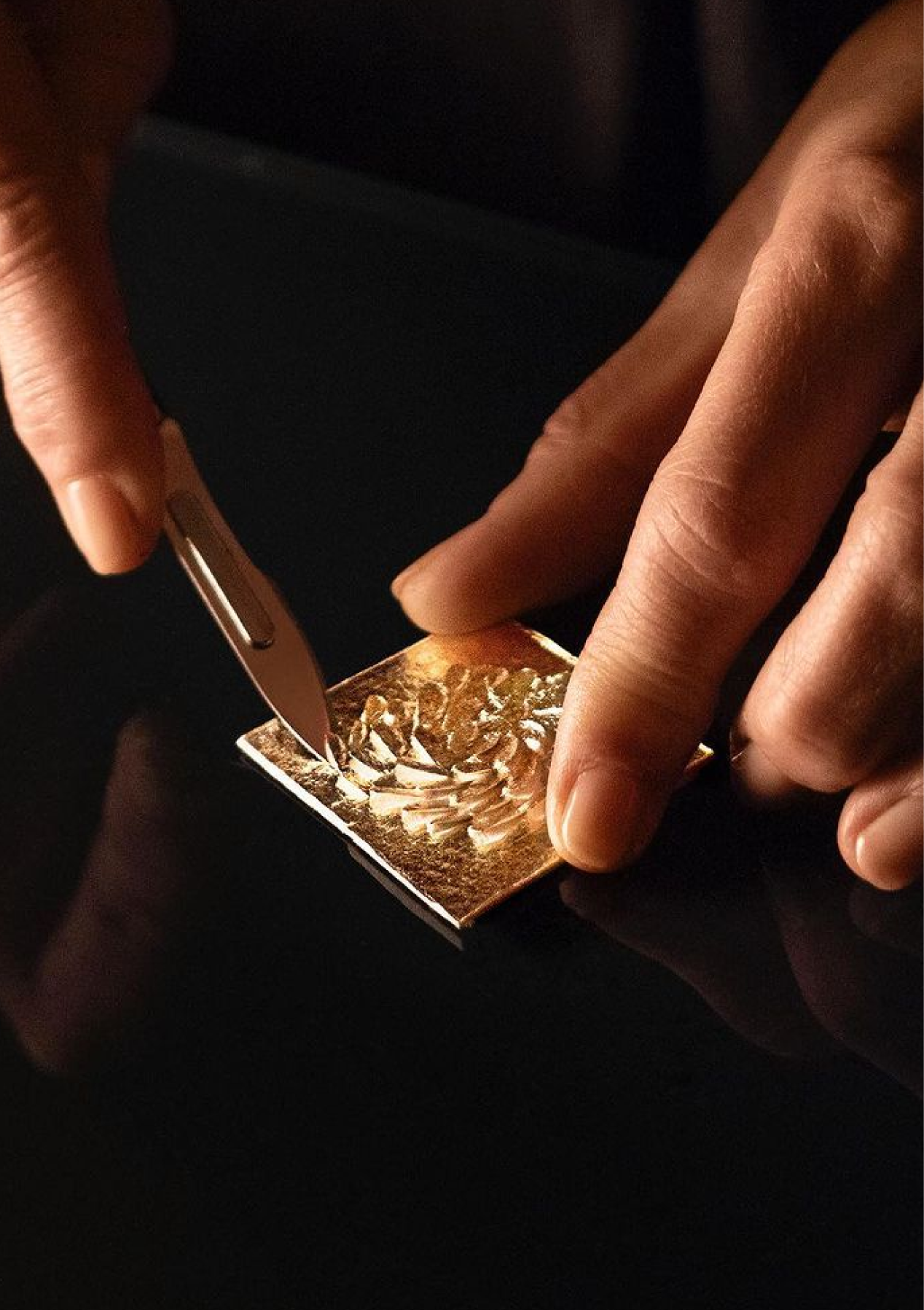 Person cutting a square of brass with a knife on a dark background