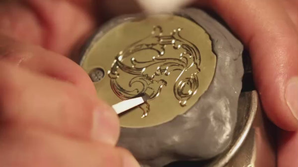 A close-up video of a man hand-engraving a monogram design in brass for a wedding invitation.